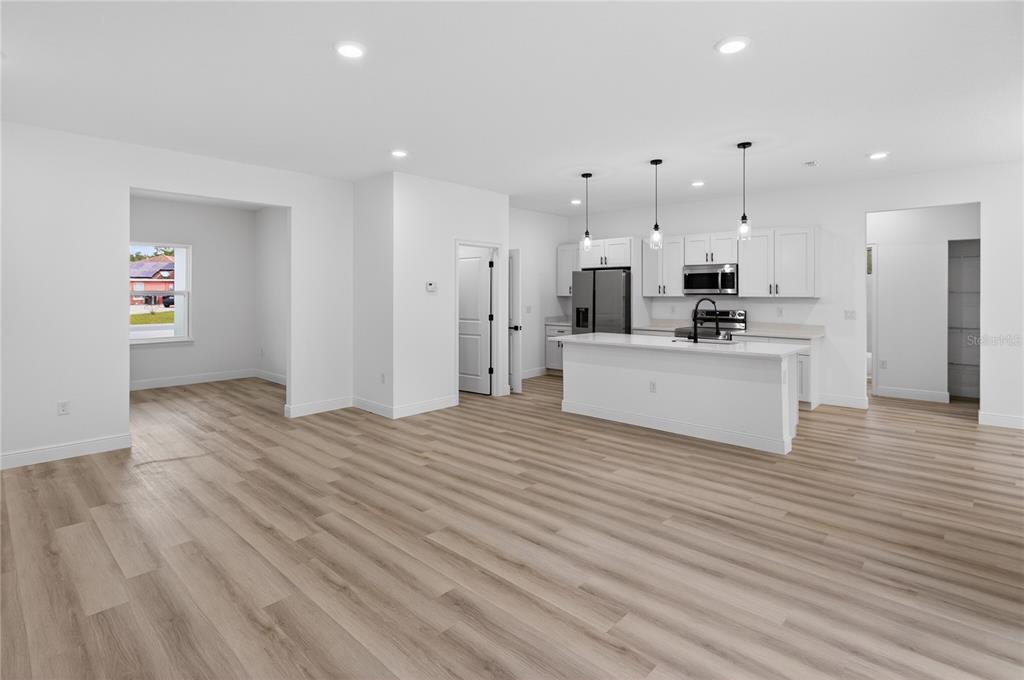 An open-concept kitchen and living area featuring white cabinetry, a center island, and wood-look flooring — 15028 SW 25TH CIRCLE, OCALA, FL