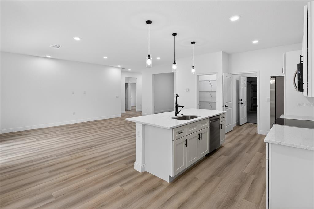 A modern kitchen features a white island with a sink, pendant lights, and light flooring — 15028 SW 25TH CIRCLE, OCALA, FL
