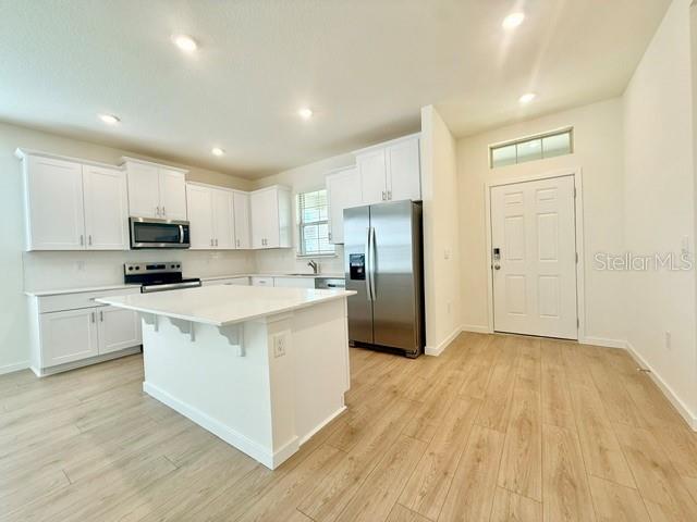 A modern kitchen features white cabinets, stainless steel appliances, a center island, and wood-look flooring — 16840 HOBE SOUND COURT, WINTER GARDEN, FL