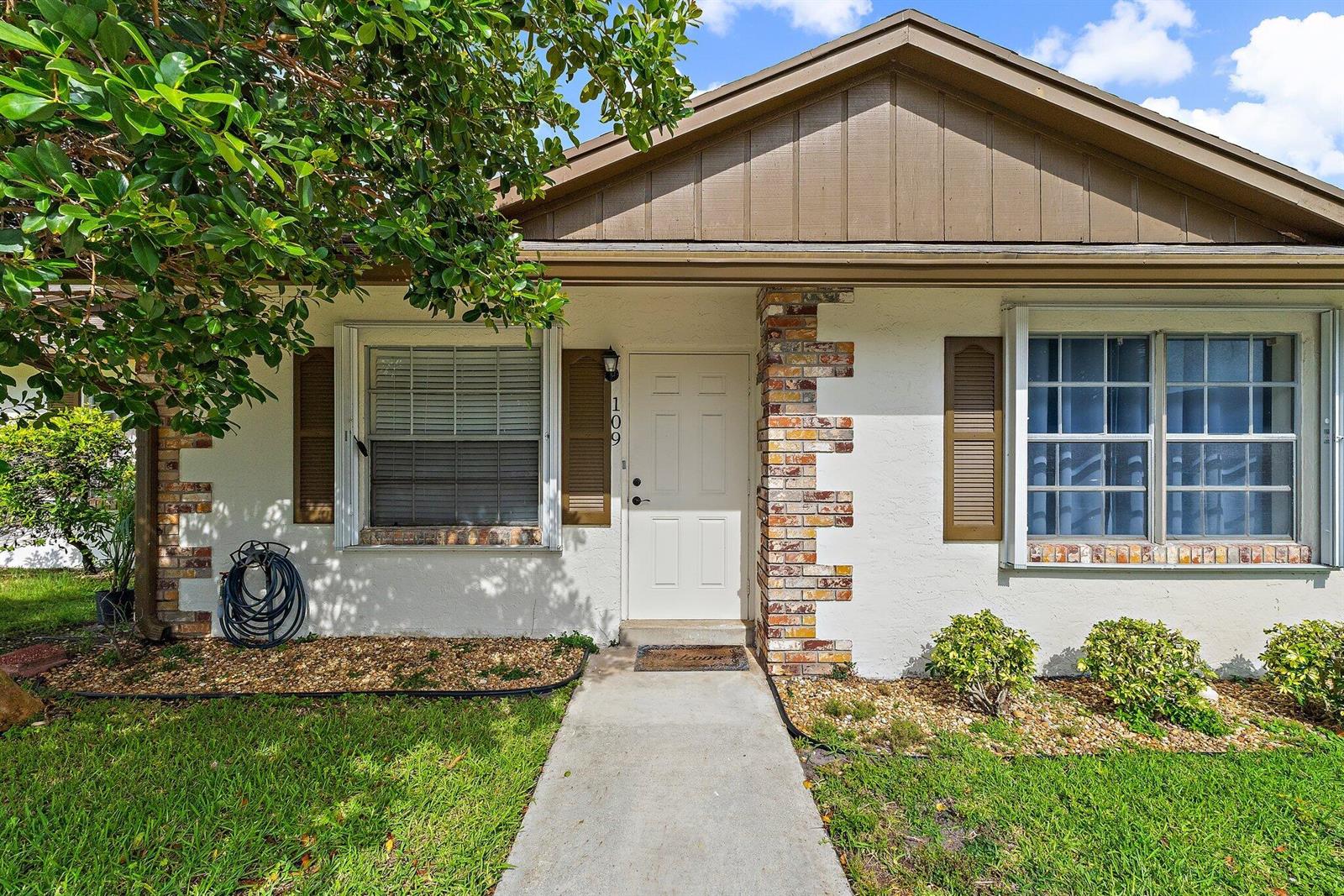 A single-story house exterior features a white stucco facade, brick accents, and a front walkway — 109 Doe Trail, Jupiter FL 33458, JUPITER, FL
