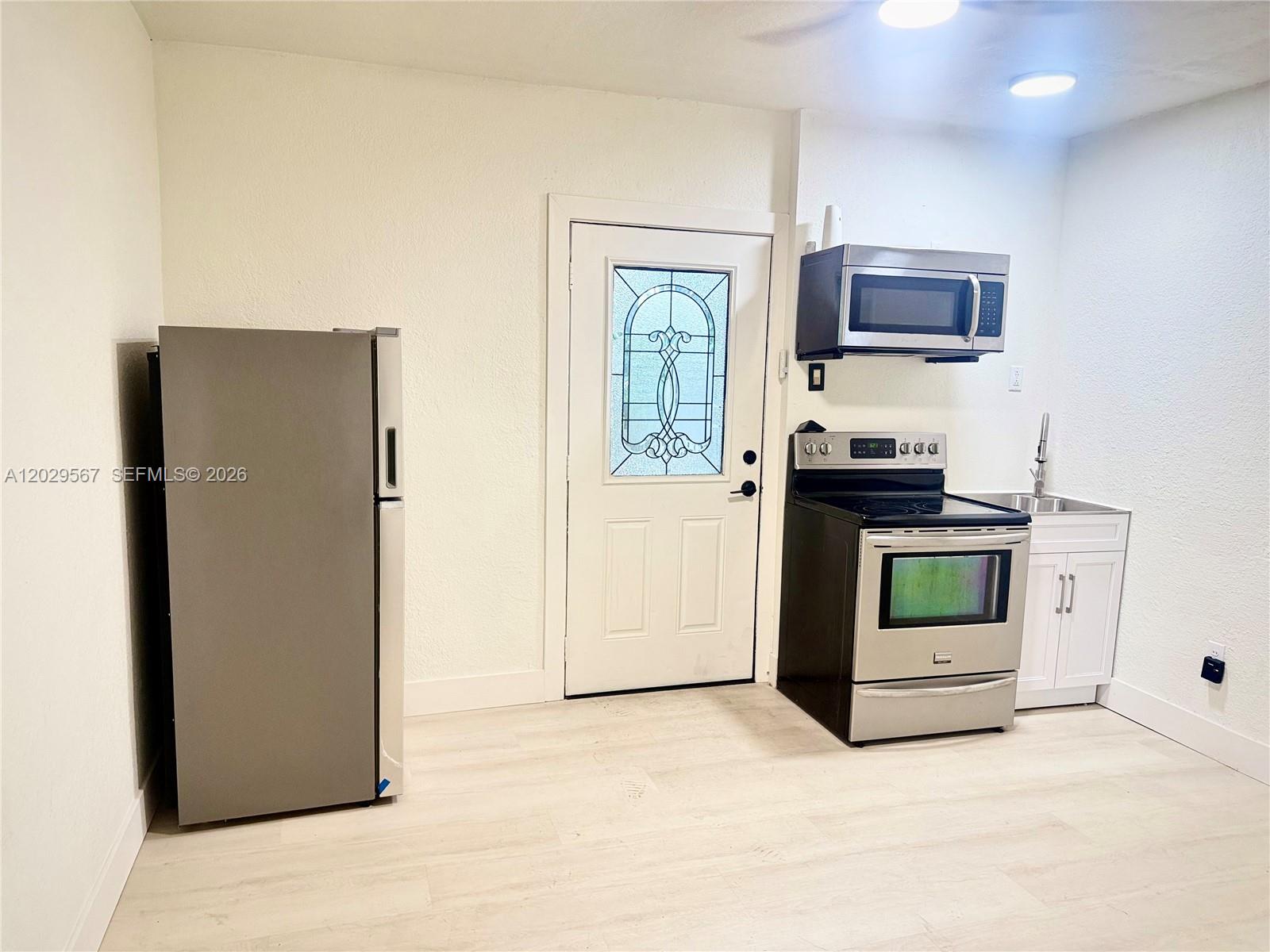 A small kitchen features stainless steel appliances, white cabinets, and light-colored flooring — 620 NE 160th St, Miami FL 33162, MIAMI, FL