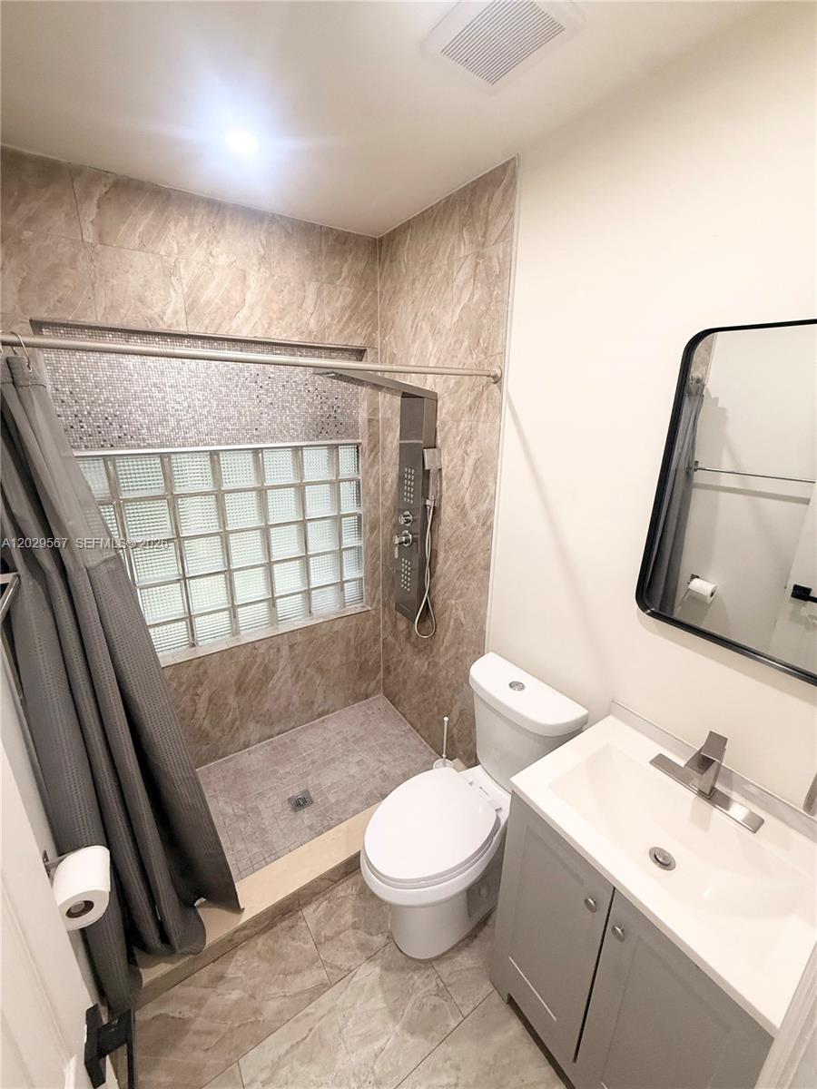 A bathroom features a tiled walk-in shower with a glass block window and gray vanity — 620 NE 160th St, Miami FL 33162, MIAMI, FL