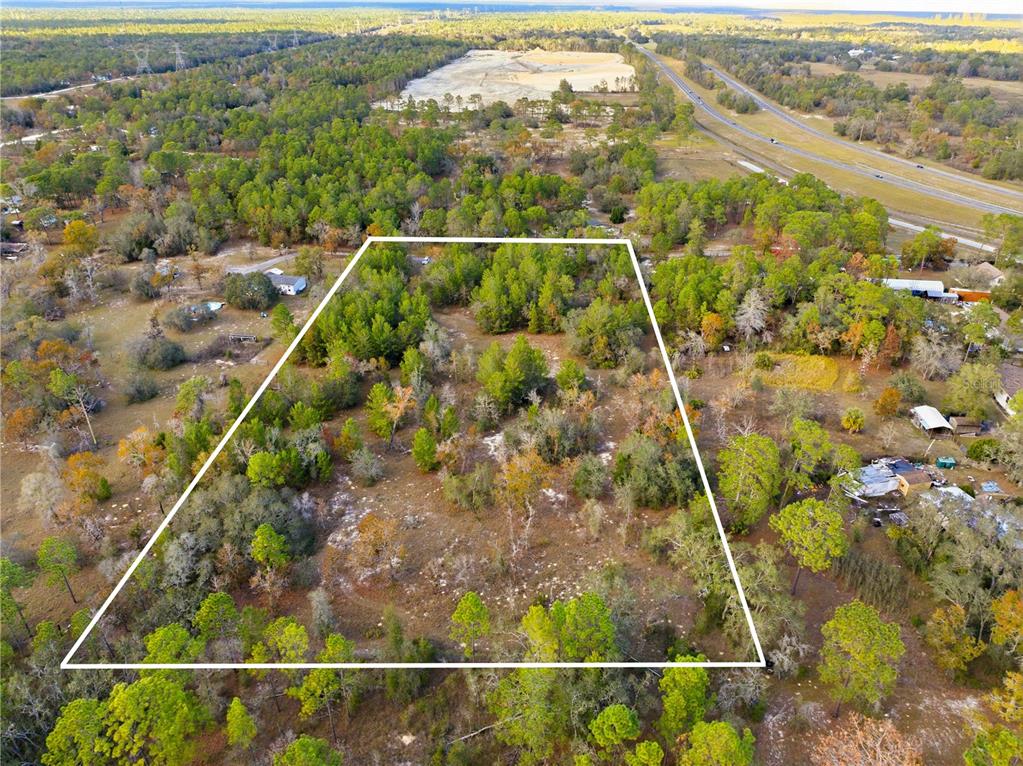 An aerial view shows a rectangular plot of land outlined in white amidst wooded surroundings — 0 BACKWOODS WAY, BROOKSVILLE, FL