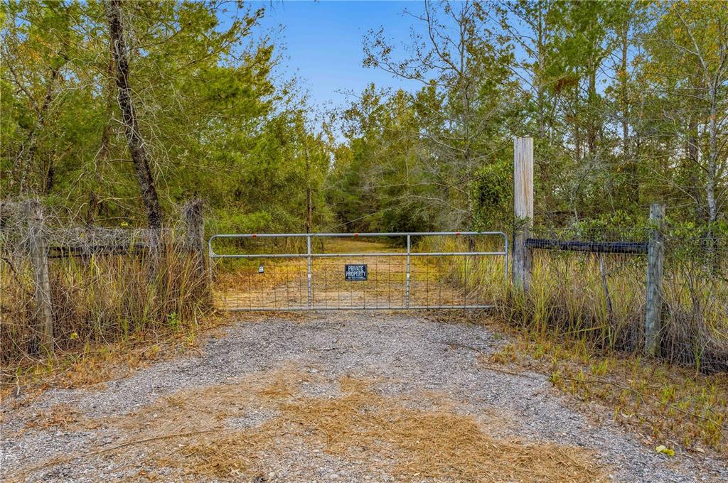 A metal gate blocks a gravel driveway leading into a wooded area — 0 BACKWOODS WAY, BROOKSVILLE, FL