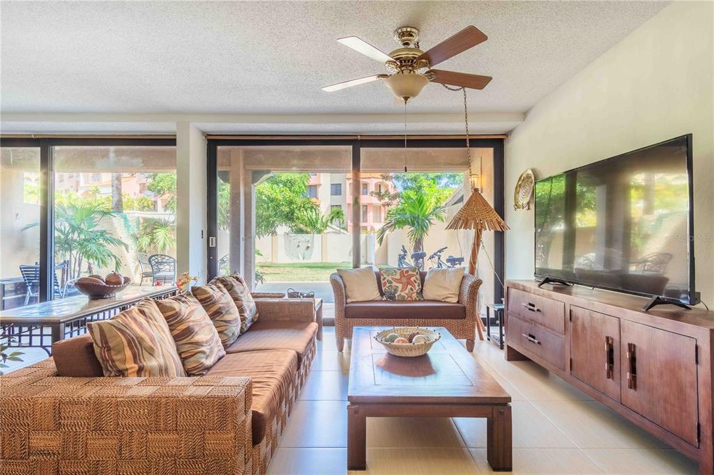 A living room with a brown sofa, wicker loveseat, wooden coffee table, and sliding glass doors — 1009 HARBOURSIDE, HUMACAO, PR