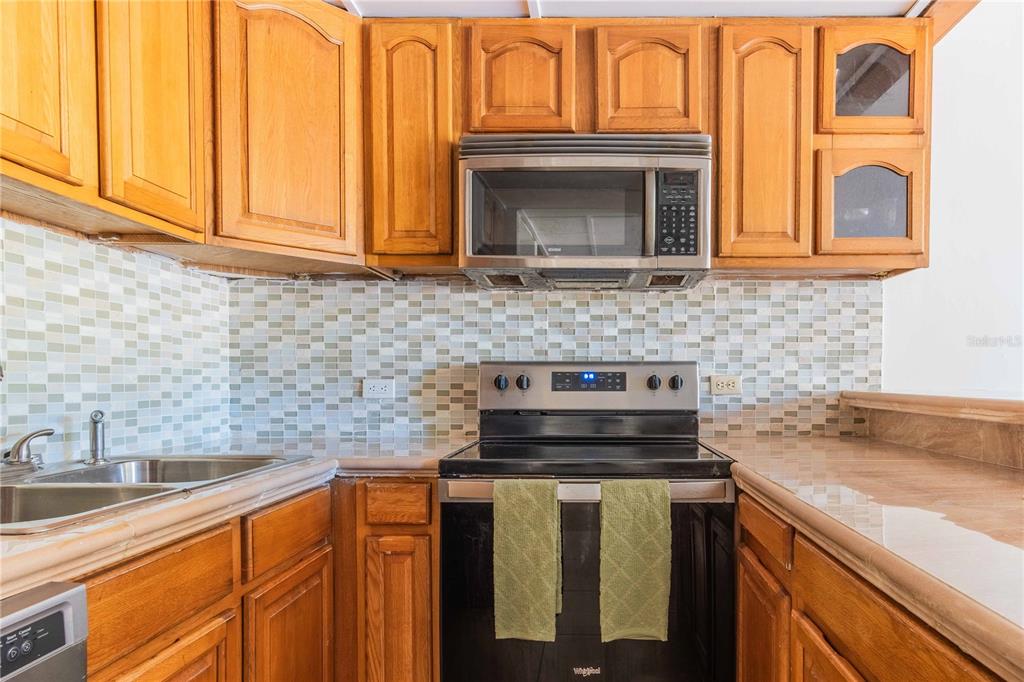A kitchen features wood cabinets, a stainless steel microwave, a black stove, and tiled backsplash — 1009 HARBOURSIDE, HUMACAO, PR