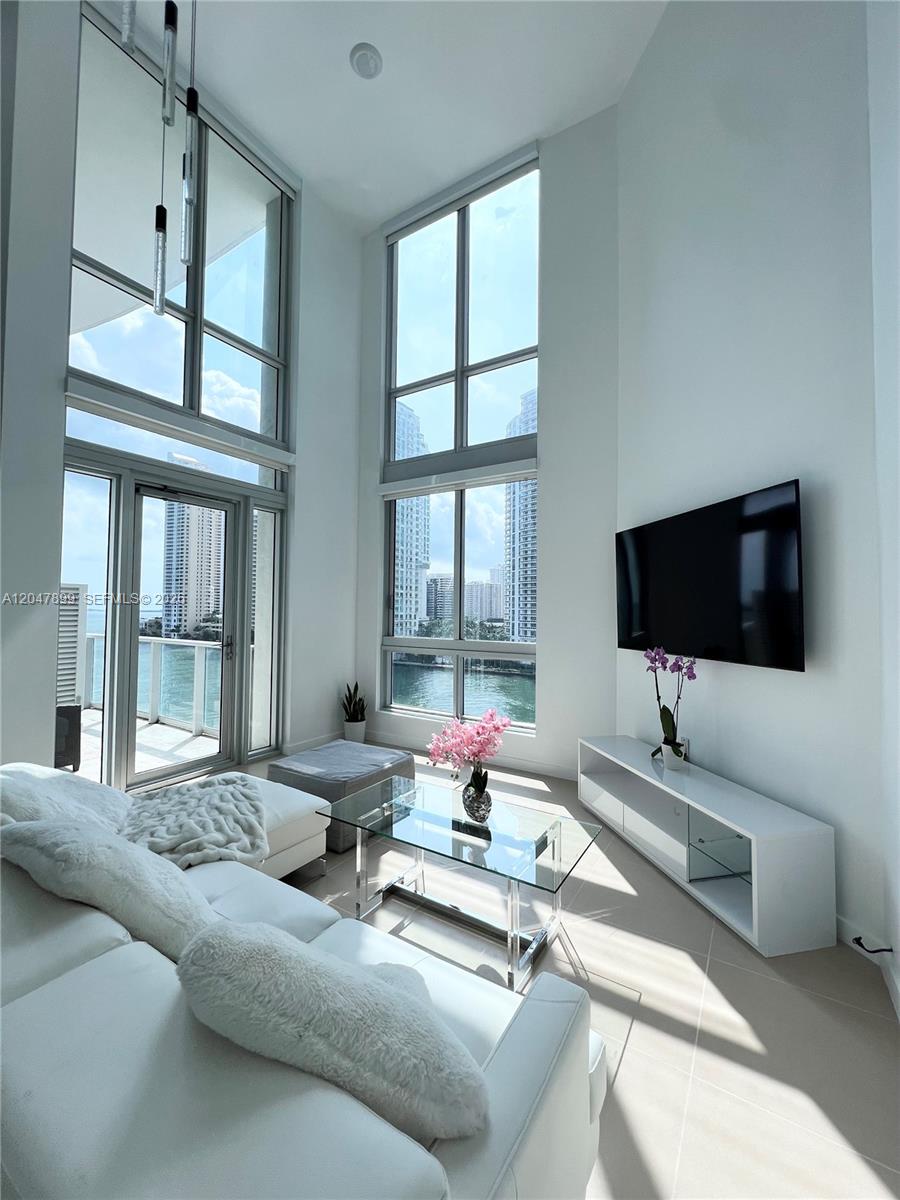 A bright living room features floor-to-ceiling windows, white furniture, and a view of water — 300 S Biscayne Blvd # 814, Miami FL 33131, MIAMI, FL