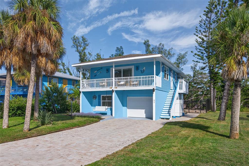 A two-story blue house with a white balcony, garage, and outdoor staircase sits on grass — 2915 AVENUE C, HOLMES BEACH, FL