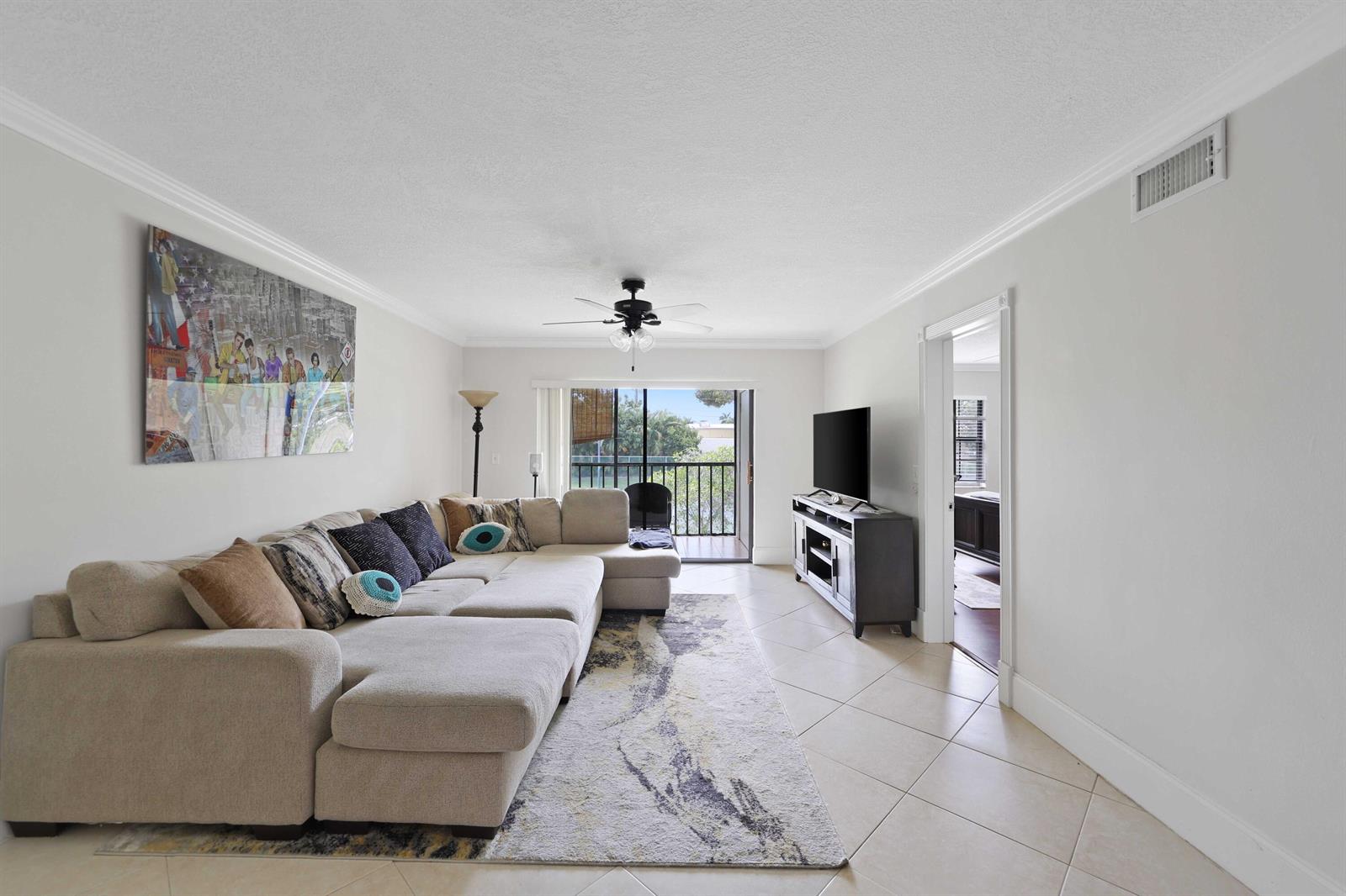 A living room features a large sectional sofa, a television console, and a balcony door — 3020 Florida Boulevard # c, Delray Beach FL 33483, DELRAY BEACH, FL