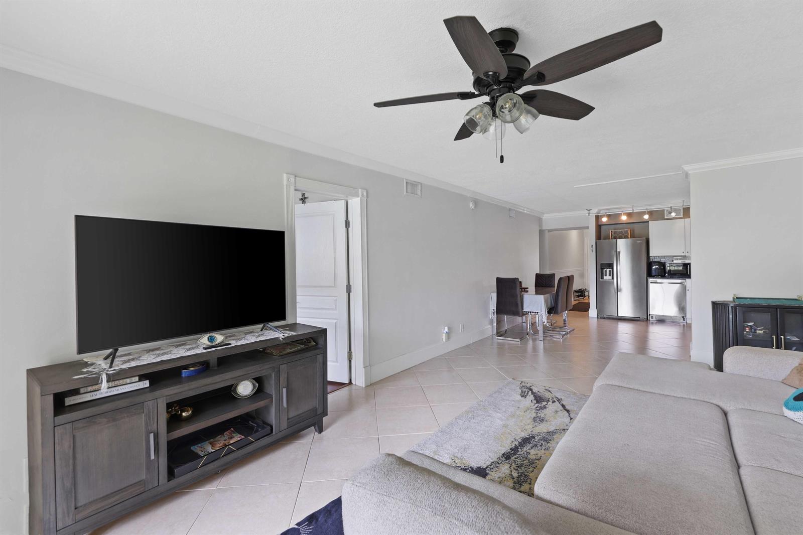 A living room with a ceiling fan, television console, and an open view to the kitchen — 3020 Florida Boulevard # c, Delray Beach FL 33483, DELRAY BEACH, FL