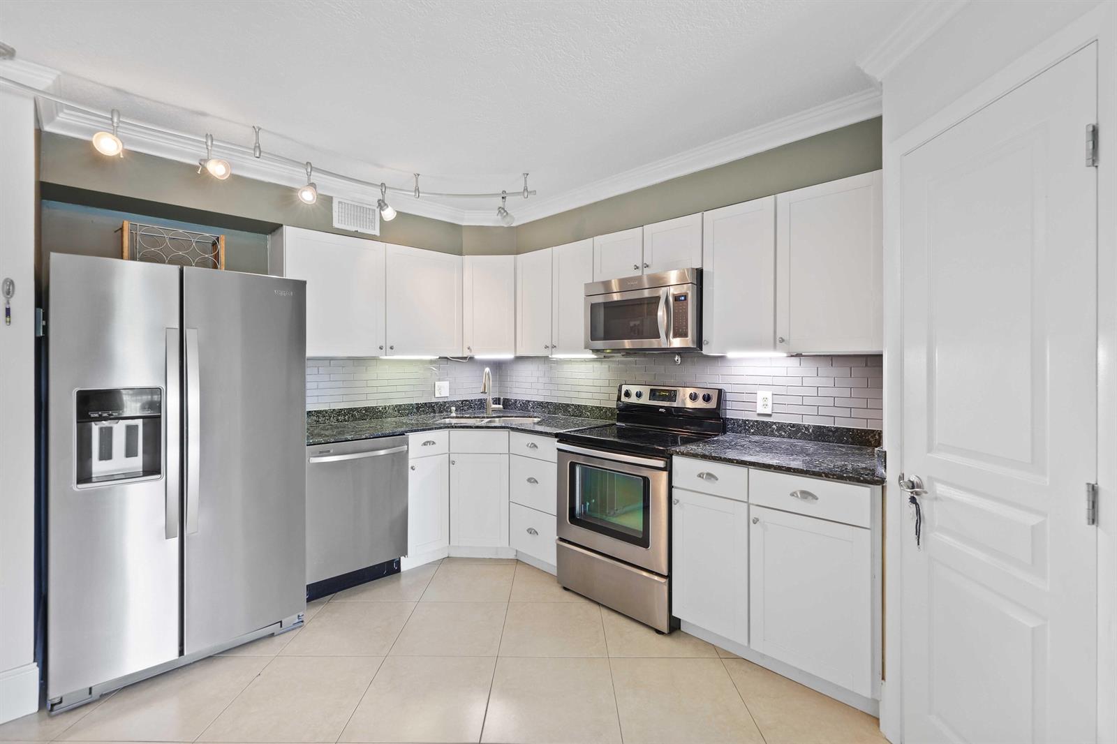 A kitchen with white cabinets, stainless steel appliances, dark granite countertops, and gray tile backsplash — 3020 Florida Boulevard # c, Delray Beach FL 33483, DELRAY BEACH, FL