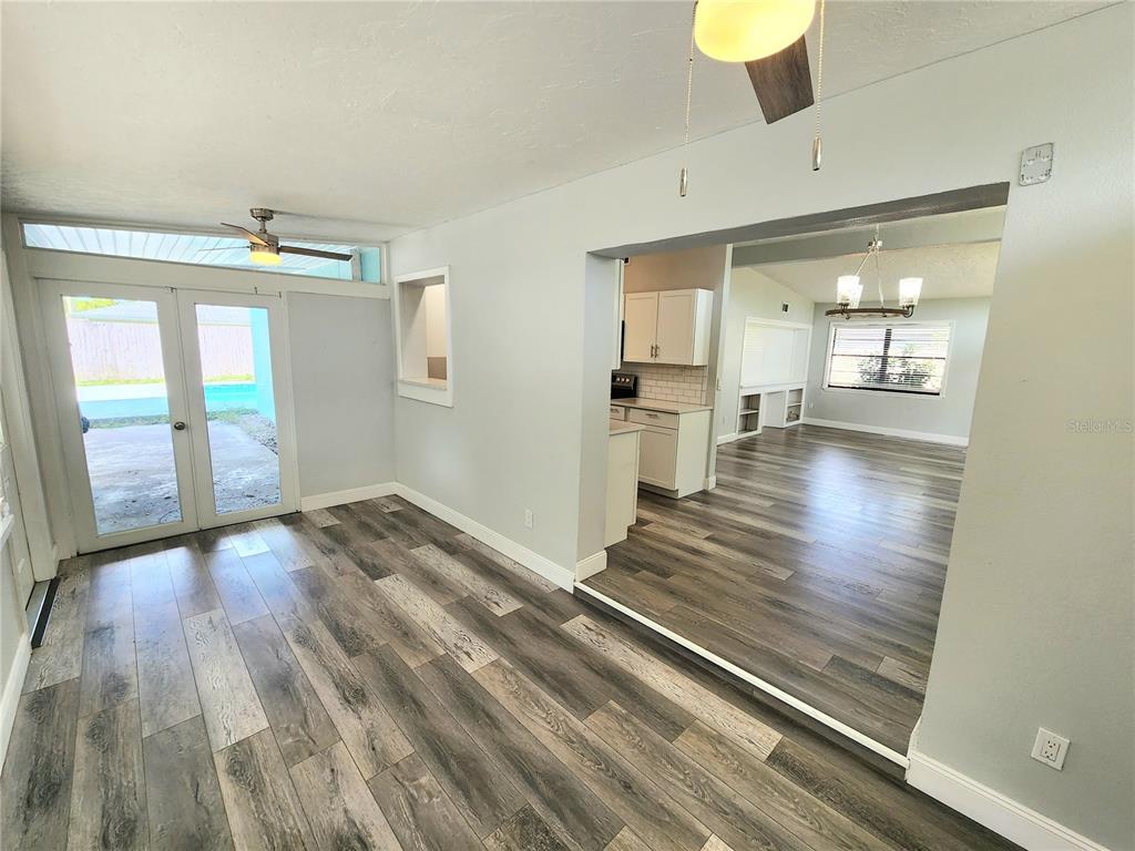 A room with wood-look flooring and French doors leading to a patio, opening into a kitchen — 2001 PRINCETON AVENUE, BRADENTON, FL
