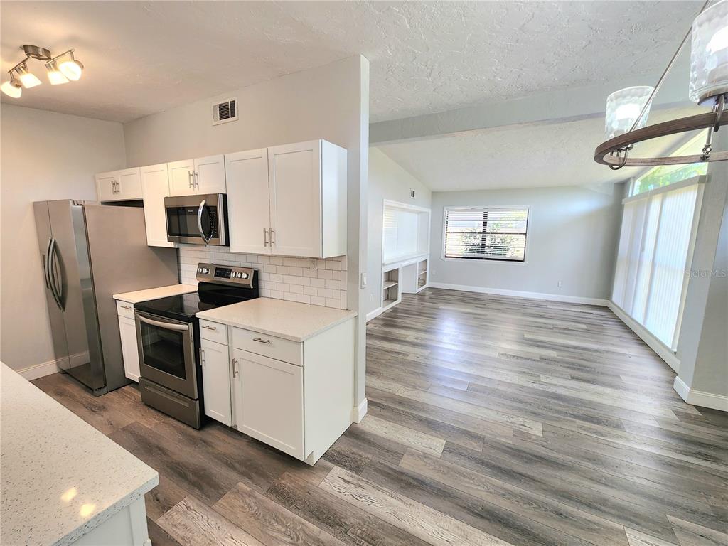 A kitchen with white cabinets and stainless steel appliances opens into a bright living area — 2001 PRINCETON AVENUE, BRADENTON, FL
