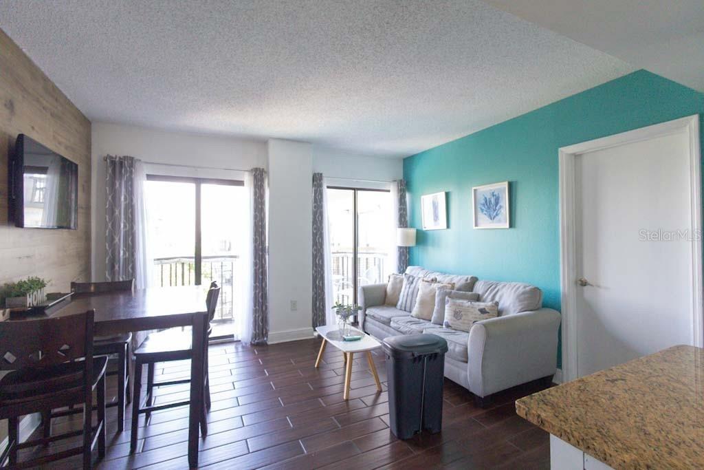 A living and dining area features dark wood-look flooring, a teal accent wall, and balcony access — 6165 CARRIER DRIVE UNIT 1601, ORLANDO, FL