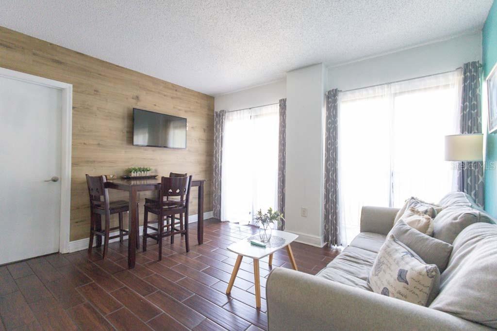 A living room features wood-look tile flooring, a wood-paneled accent wall, and a dining area — 6165 CARRIER DRIVE UNIT 1601, ORLANDO, FL
