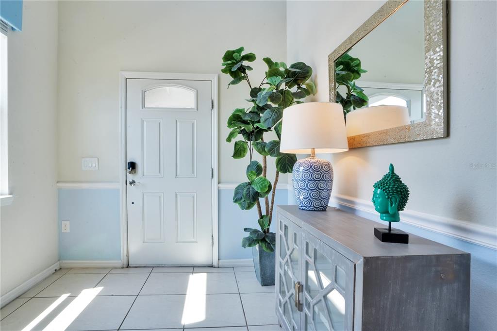 An entryway features a white door, a potted plant, a console table, and a mirror — 8936 PRAGUE WAY, KISSIMMEE, FL