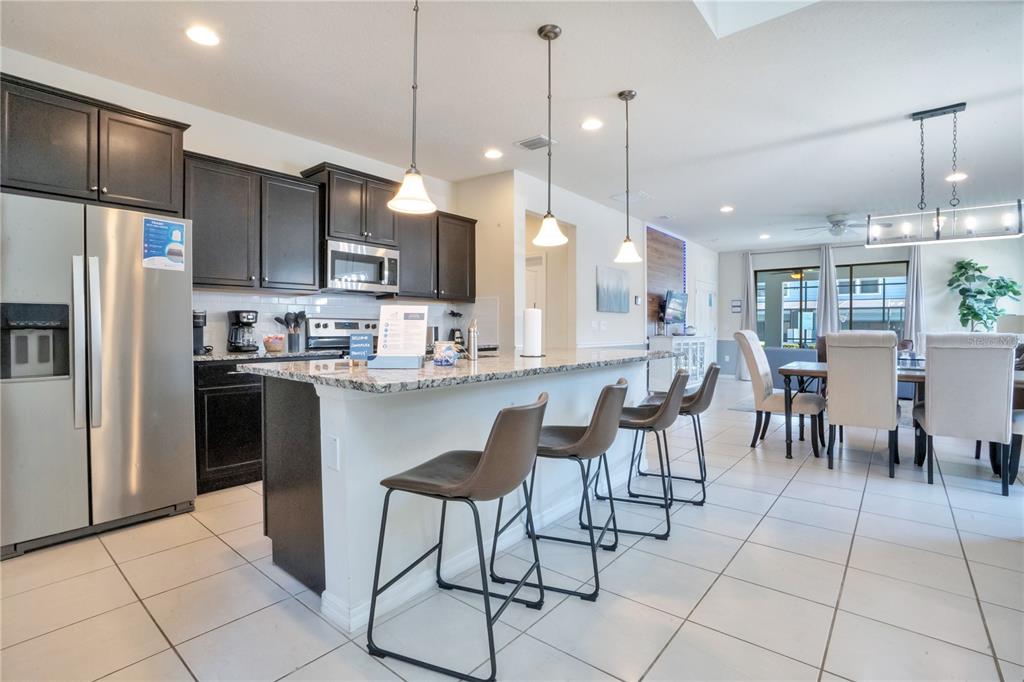 A kitchen with dark cabinets, granite countertops, a breakfast bar, and an adjacent dining area — 8936 PRAGUE WAY, KISSIMMEE, FL
