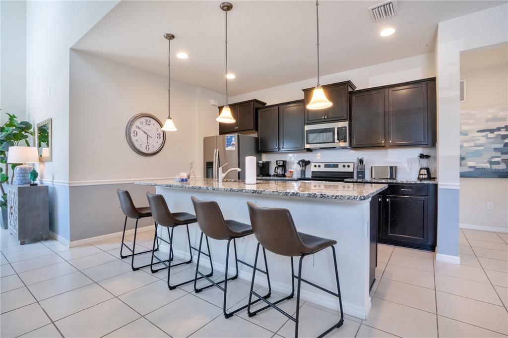 A kitchen features dark cabinets, granite countertops, a breakfast bar with four stools, and tile flooring — 8936 PRAGUE WAY, KISSIMMEE, FL