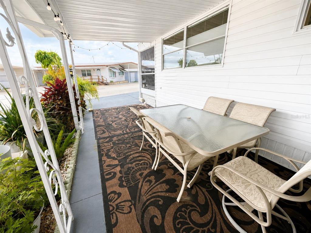 A covered patio features a glass-top dining table with chairs on a patterned outdoor rug — 1613 MICHIGAN AVENUE, BRADENTON, FL