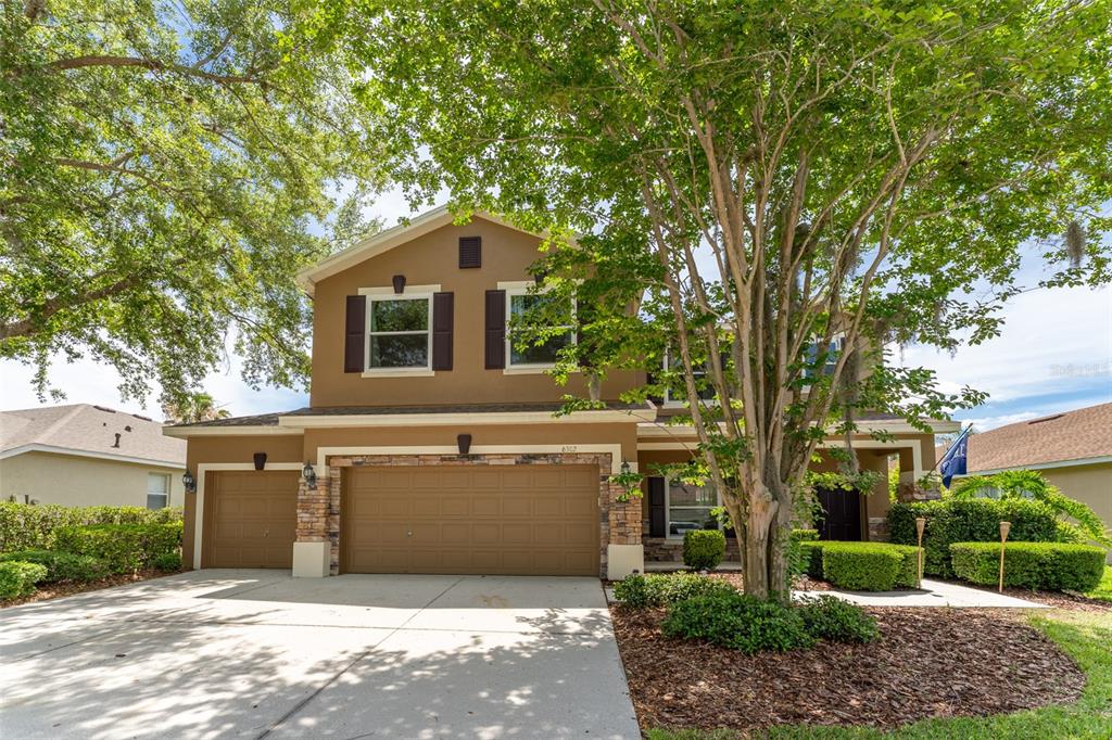 A two-story house with a tan stucco exterior, stone accents, and a three-car garage — 6302 BRIDGEVISTA DRIVE, LITHIA, FL