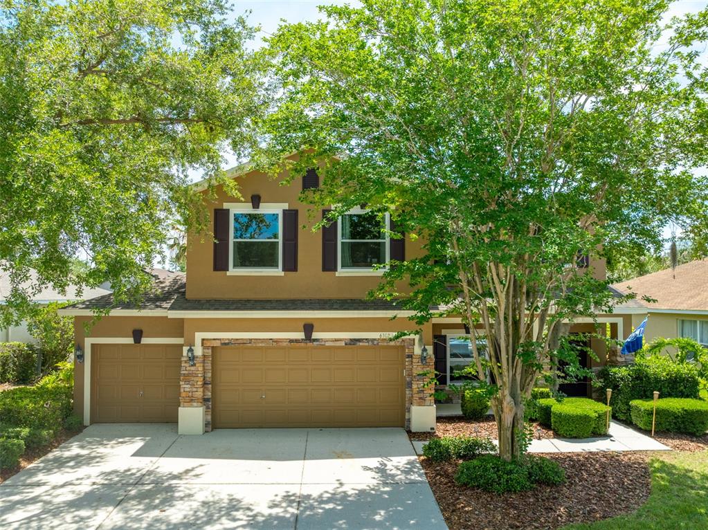 A two-story house with a tan stucco exterior, stone accents, and a three-car garage — 6302 BRIDGEVISTA DRIVE, LITHIA, FL