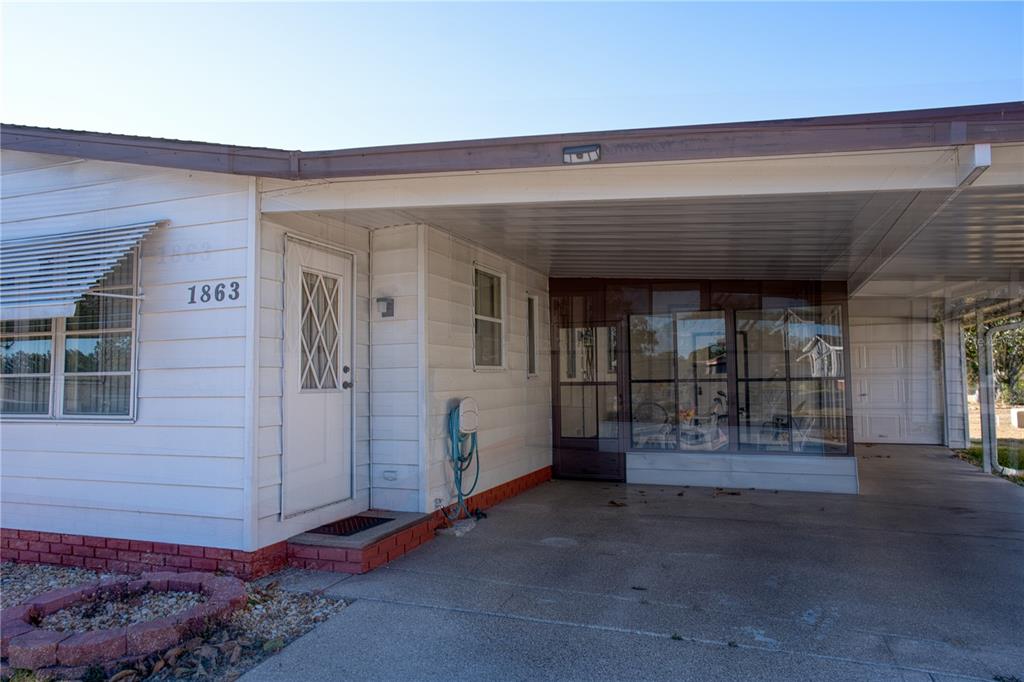 A white mobile home exterior features a carport, a glass-enclosed porch, and a brick border — 1863 W SCHWARTZ BOULEVARD, LADY LAKE, FL
