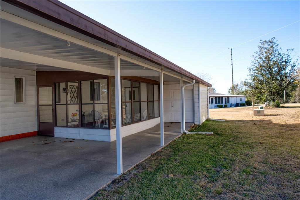 A covered concrete carport extends alongside a screened-in porch on a residential home — 1863 W SCHWARTZ BOULEVARD, LADY LAKE, FL