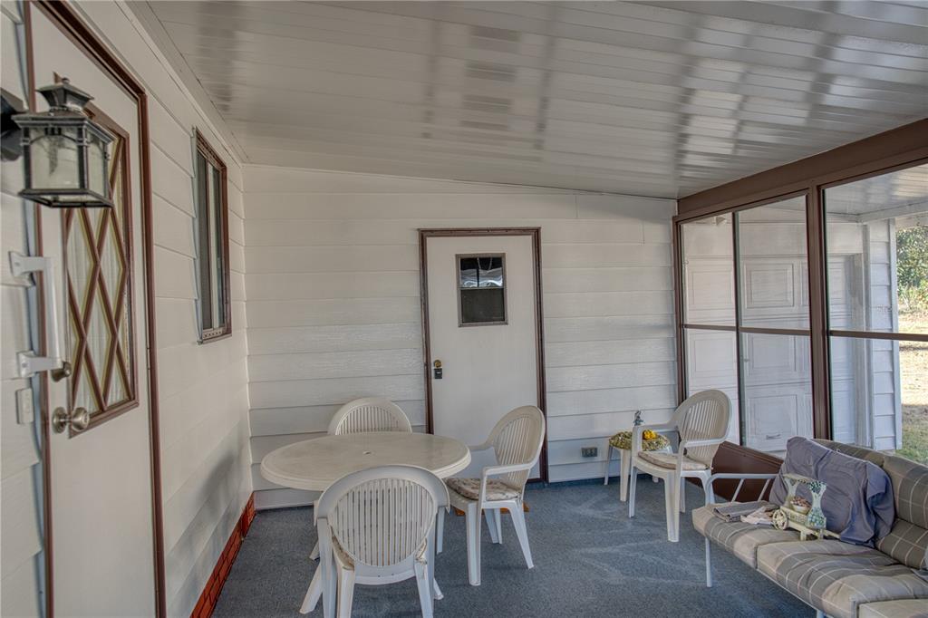 A screened-in porch features white horizontal siding, a gray carpeted floor, and patio furniture — 1863 W SCHWARTZ BOULEVARD, LADY LAKE, FL