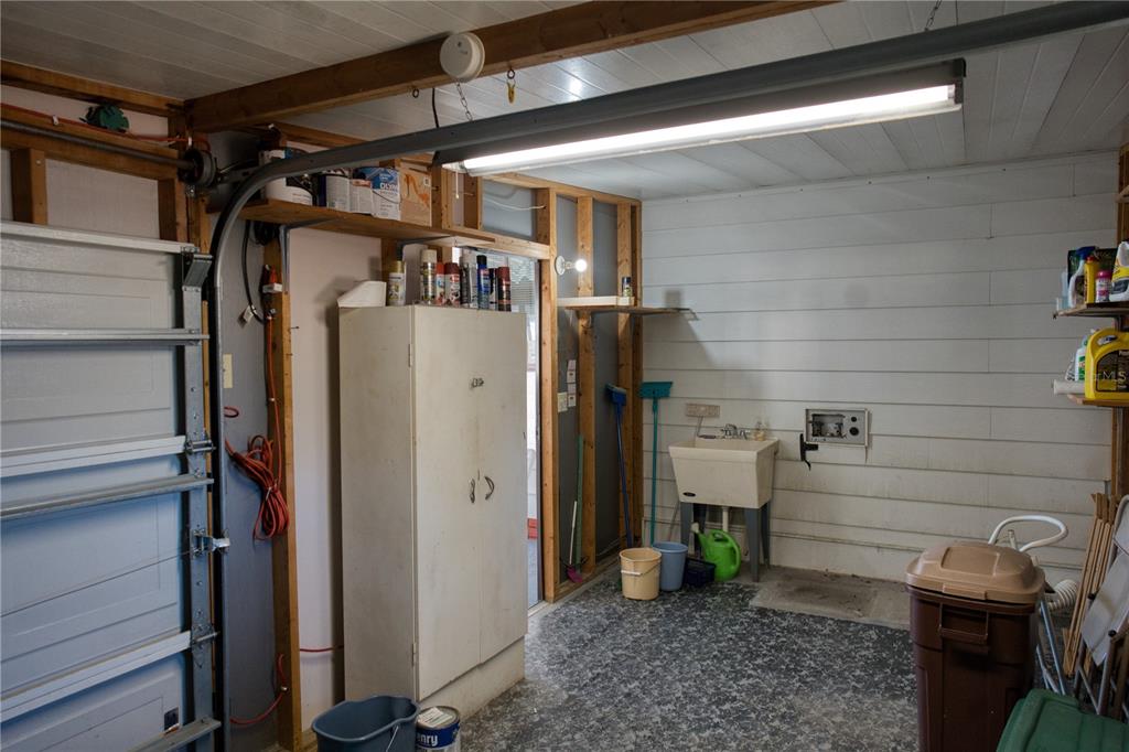A garage interior features a utility sink, storage cabinet, exposed wall studs, and concrete flooring — 1863 W SCHWARTZ BOULEVARD, LADY LAKE, FL