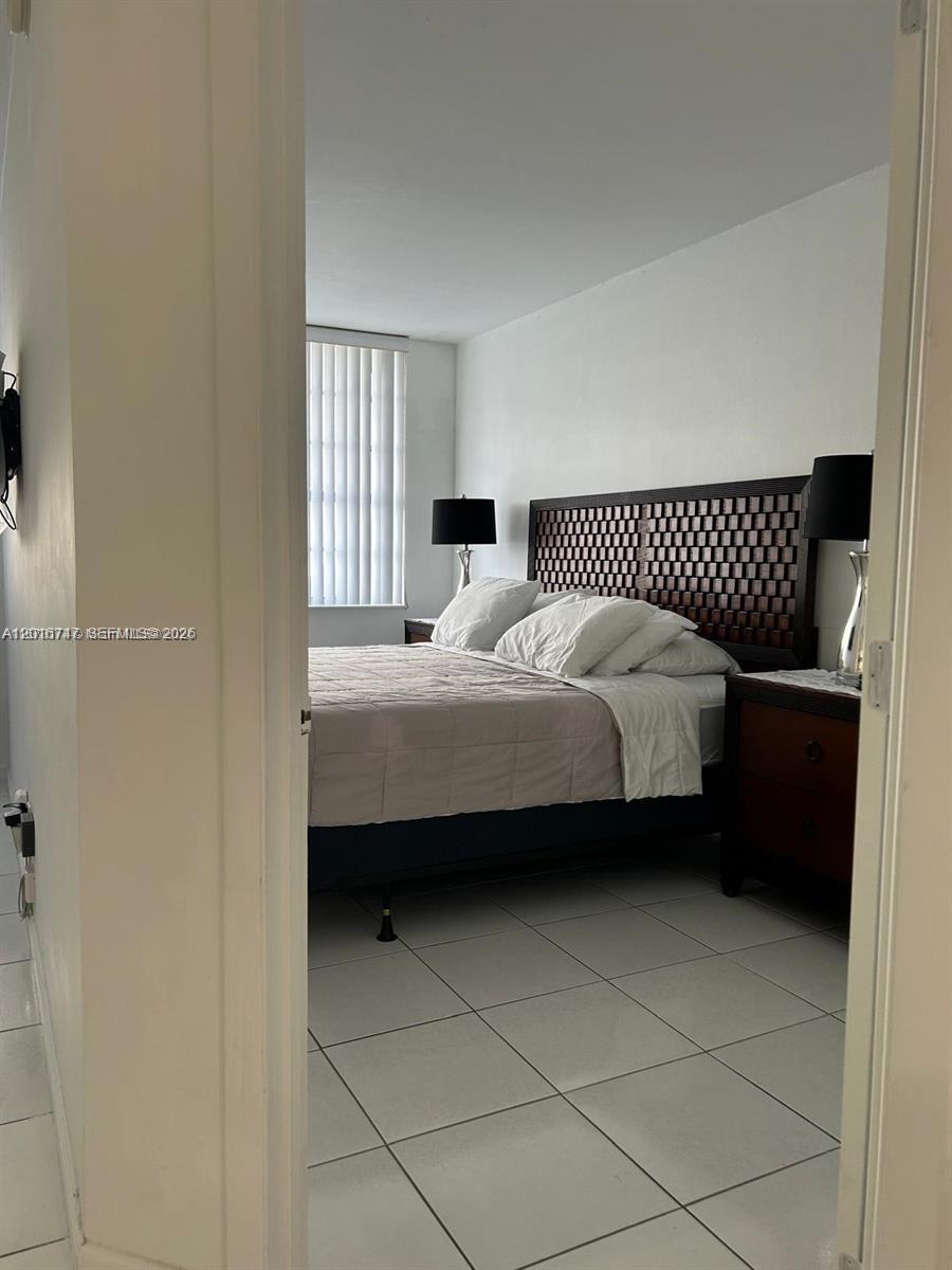 A bedroom features a dark wooden headboard, two bedside lamps, and light-colored tile flooring — 100 Lincoln Rd # 437, Miami Beach FL 33139, MIAMI BEACH, FL