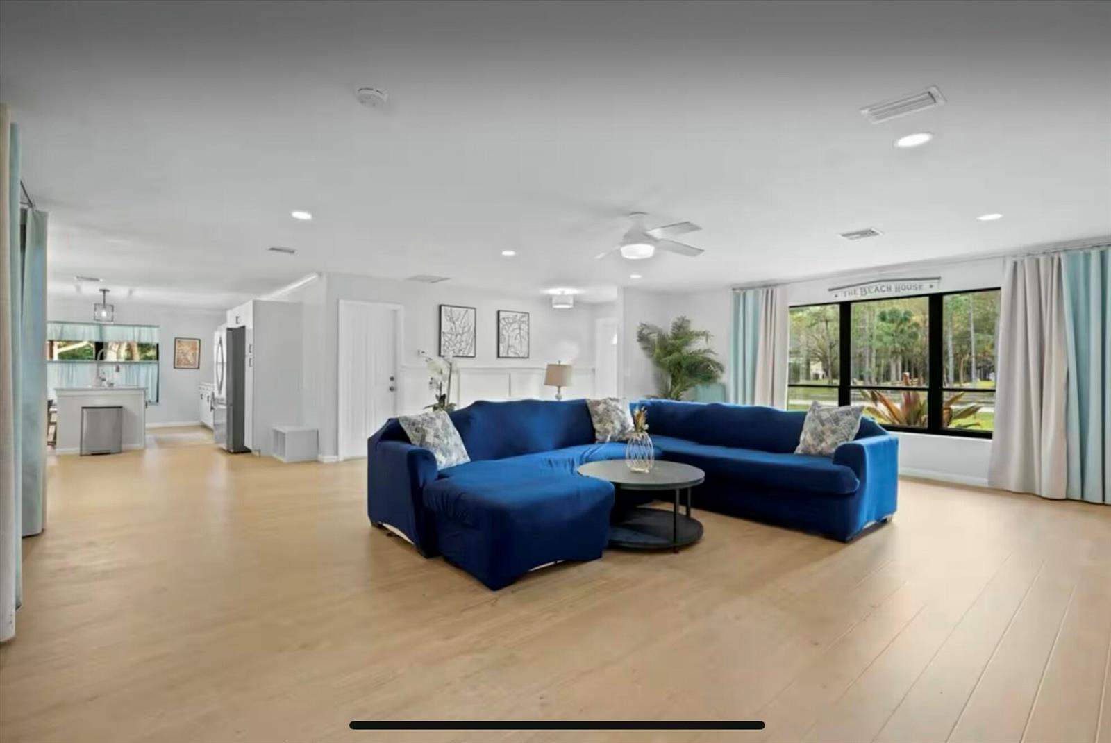 A spacious living room features light wood flooring, a large blue sectional, and a kitchen — 11405 N 175th Rd Road N, FL 33478, FL