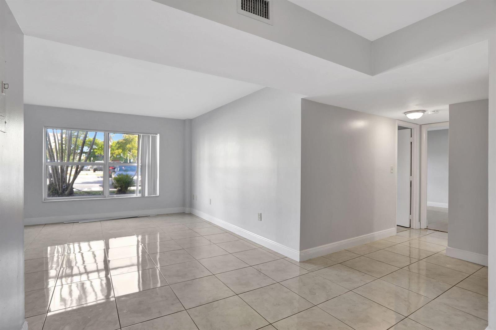 An empty room with light gray walls, large windows, and beige tile flooring — 4156 Inverrary Drive # 111, Lauderhill FL 33319, LAUDERHILL, FL