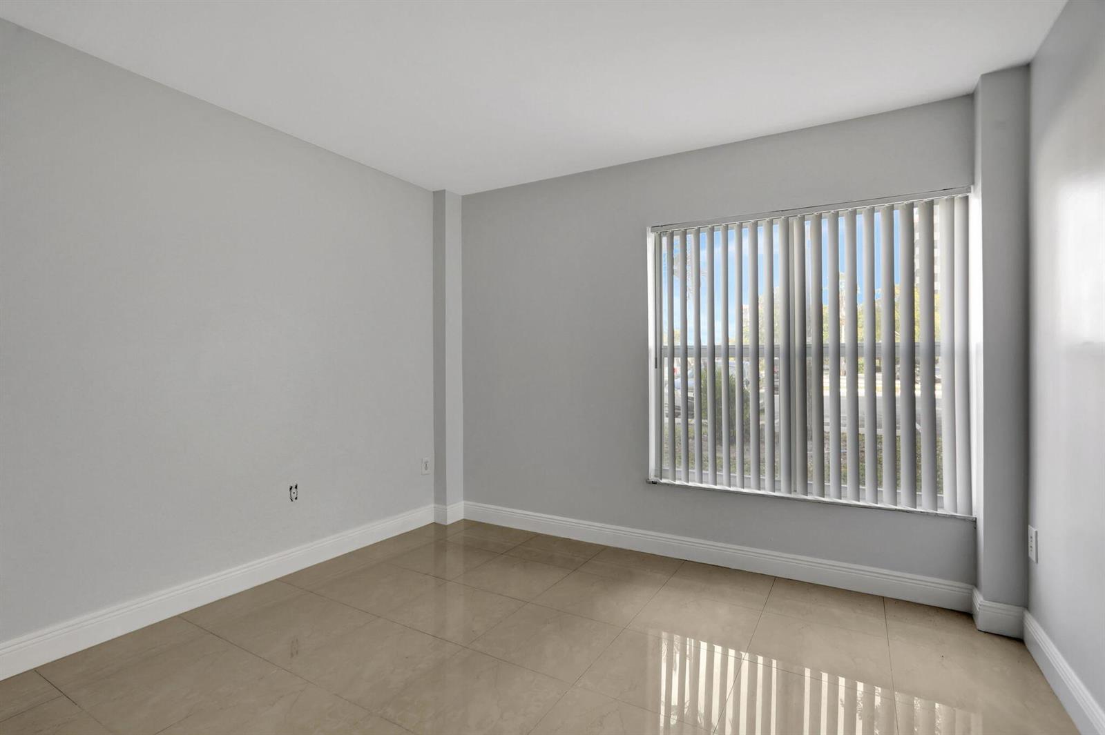 An empty room features light gray walls, large beige floor tiles, and a window with blinds — 4156 Inverrary Drive # 111, Lauderhill FL 33319, LAUDERHILL, FL