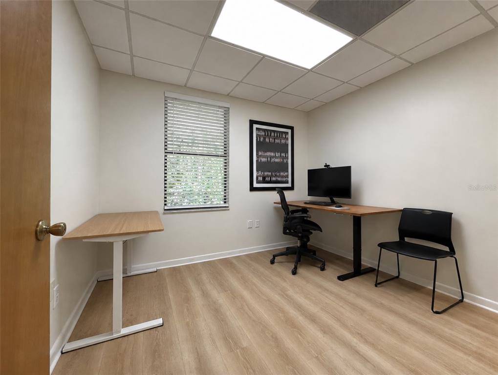 A home office features light wood flooring, two desks, a black office chair, and a window — 2731 NW 41ST STREET UNIT B2, GAINESVILLE, FL