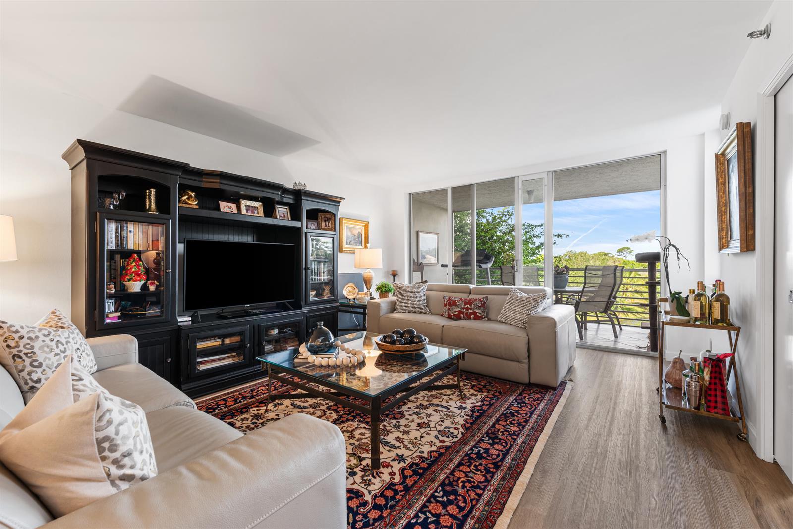 A living room features a large black entertainment center, two light-colored sofas, and a balcony view — 3499 Oaks Way # 407, Pompano Beach FL 33069, POMPANO BEACH, FL
