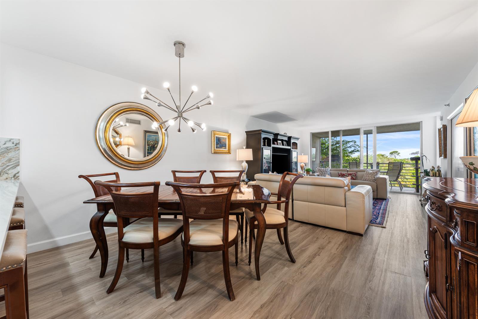 A dining area with a modern chandelier and wooden furniture opens into a living room — 3499 Oaks Way # 407, Pompano Beach FL 33069, POMPANO BEACH, FL