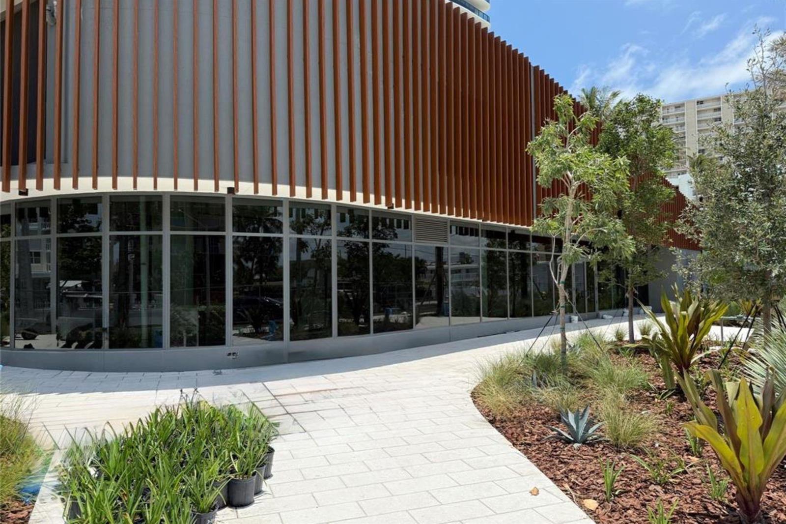 A curved building exterior features floor-to-ceiling glass windows and vertical brown architectural slats — 900 N Ocean Boulevard, Pompano Beach FL 33062, POMPANO BEACH, FL
