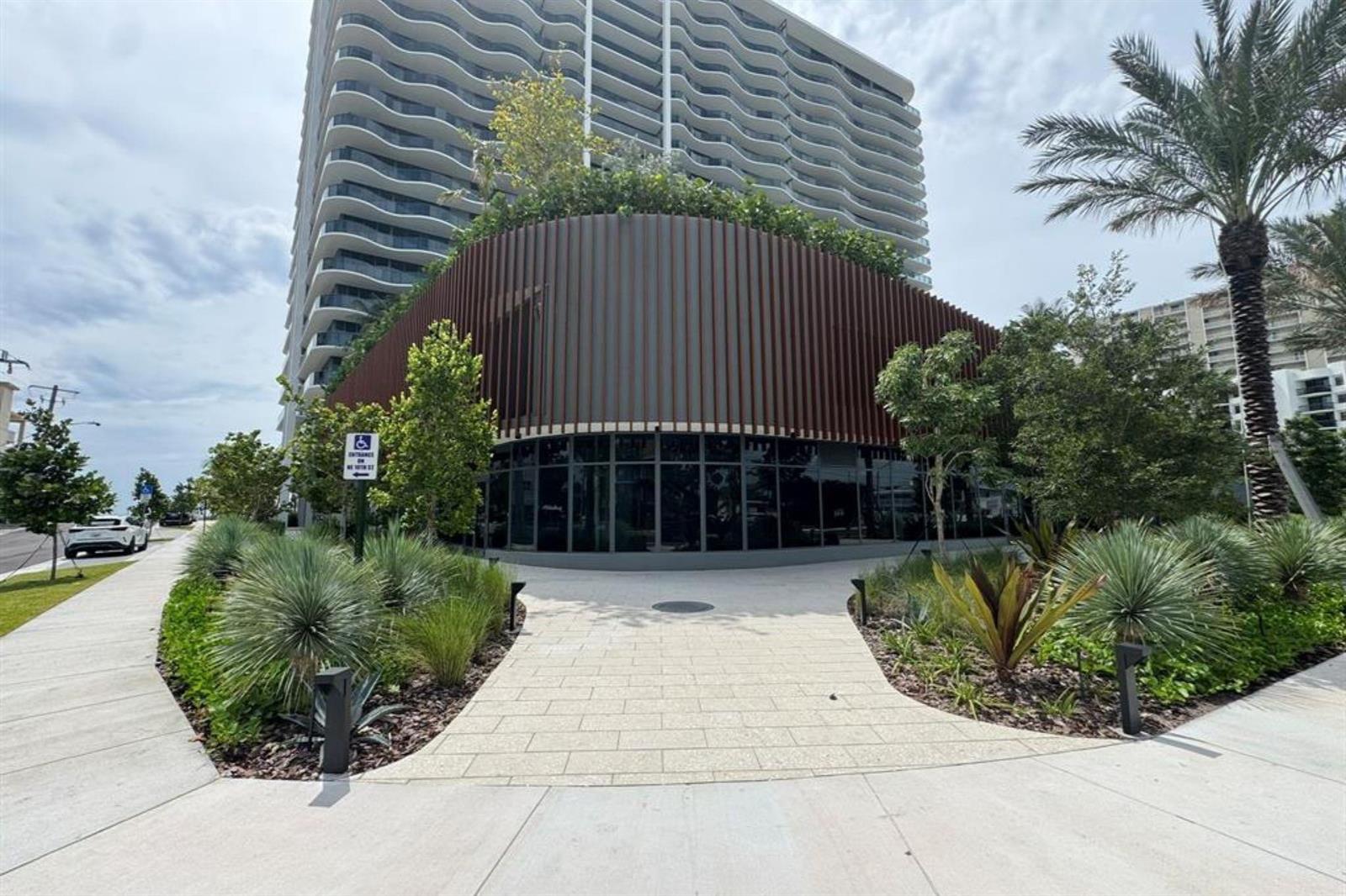 A modern high-rise building with a curved, slatted facade and landscaped pedestrian walkway — 900 N Ocean Boulevard, Pompano Beach FL 33062, POMPANO BEACH, FL