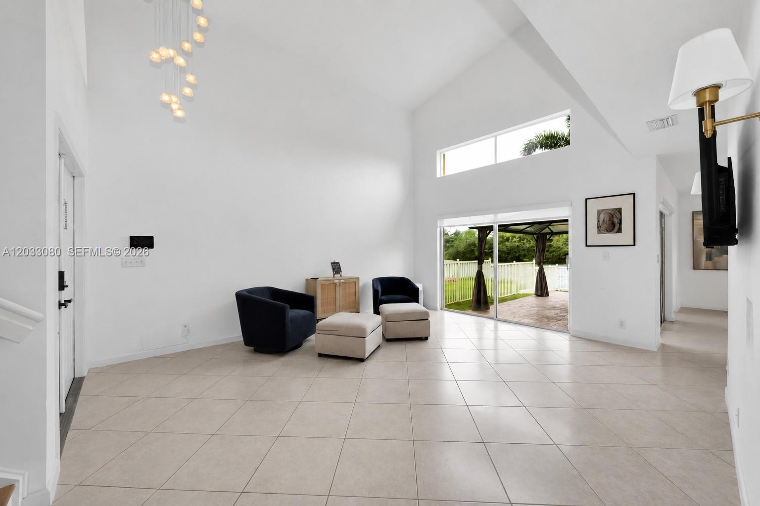 A bright living room features high vaulted ceilings, tile flooring, and a sliding glass door — 18018 SW 30th Ct, Miramar FL 33029, MIRAMAR, FL