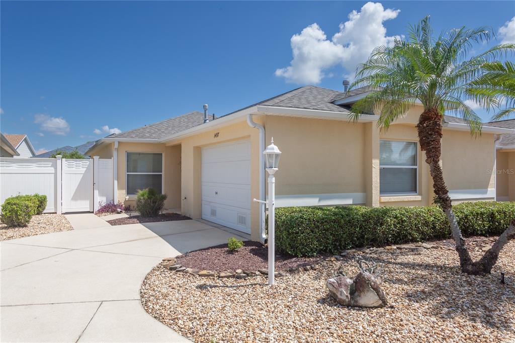 A single-story house with a garage, a palm tree, and a gravel front yard — 1497 ALEXANDRIA PLACE, THE VILLAGES, FL