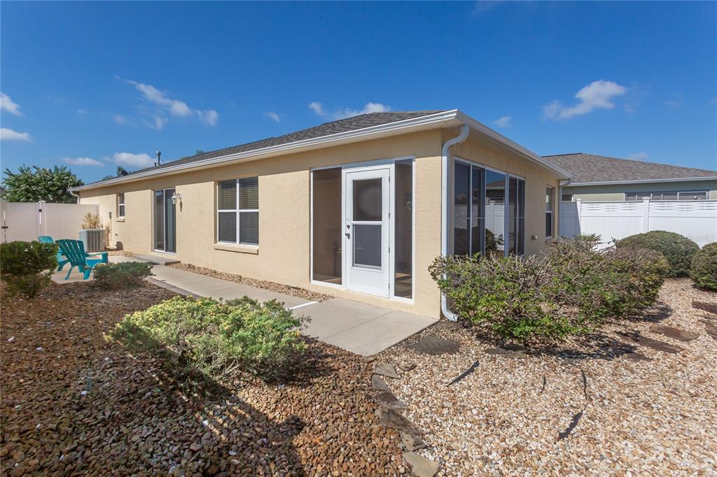 The exterior of a tan house features a screened-in porch, gravel landscaping, and blue chairs — 1497 ALEXANDRIA PLACE, THE VILLAGES, FL