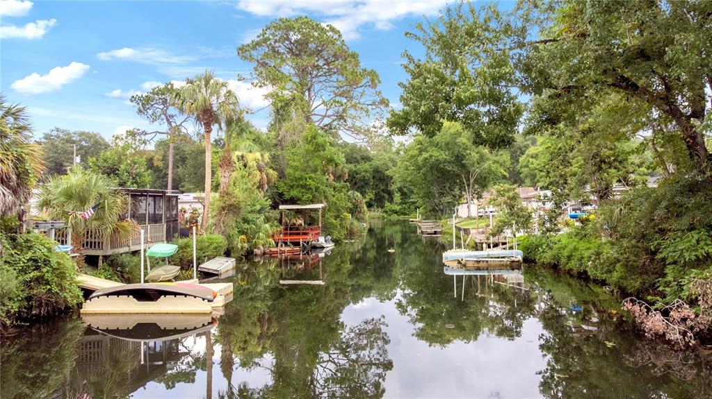 A narrow canal flows between lush green trees and residential docks with small boats — 6416 THERESA AVENUE, WEEKI WACHEE, FL