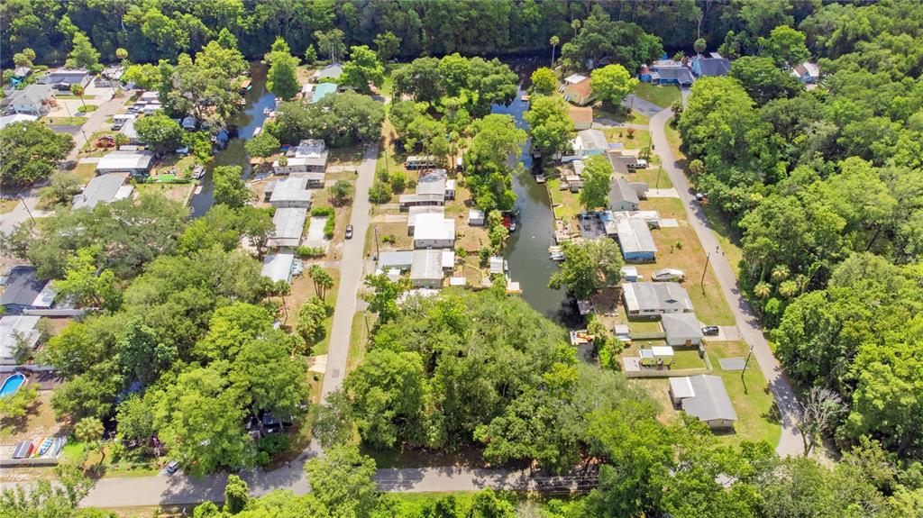 An aerial view shows houses situated along a narrow canal surrounded by dense green trees — 6416 THERESA AVENUE, WEEKI WACHEE, FL