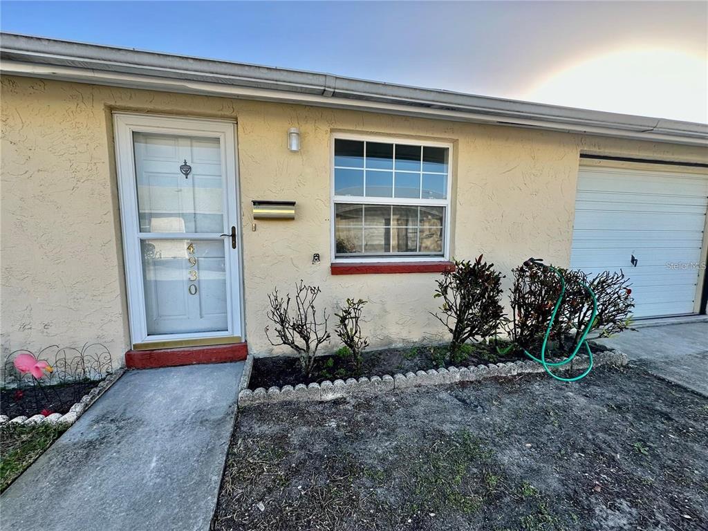The exterior of a single-story home features a front door, window, and attached garage — 4930 GETNER STREET, NEW PORT RICHEY, FL
