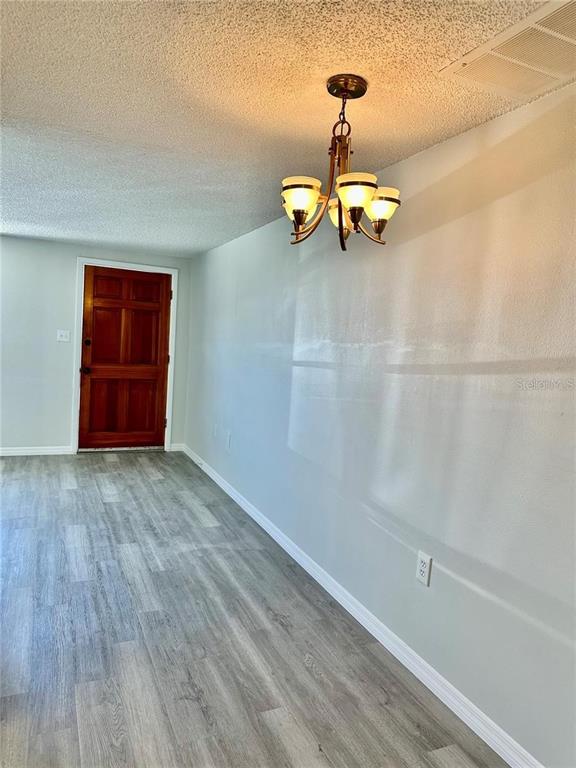 A dining area features light gray wood-look flooring, a chandelier, and a wooden front door — 4930 GETNER STREET, NEW PORT RICHEY, FL