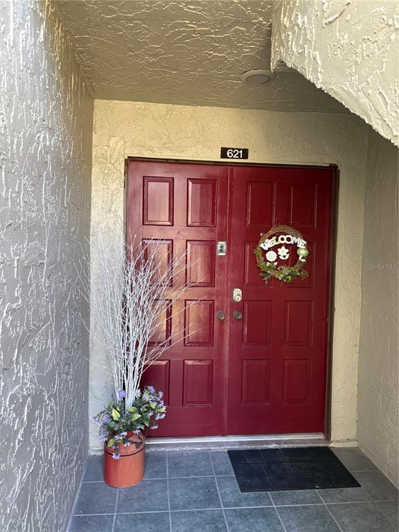 A red double front door with a wreath and a potted plant sits under a porch — 621 WINDRUSH BAY DRIVE UNIT 621, TARPON SPRINGS, FL