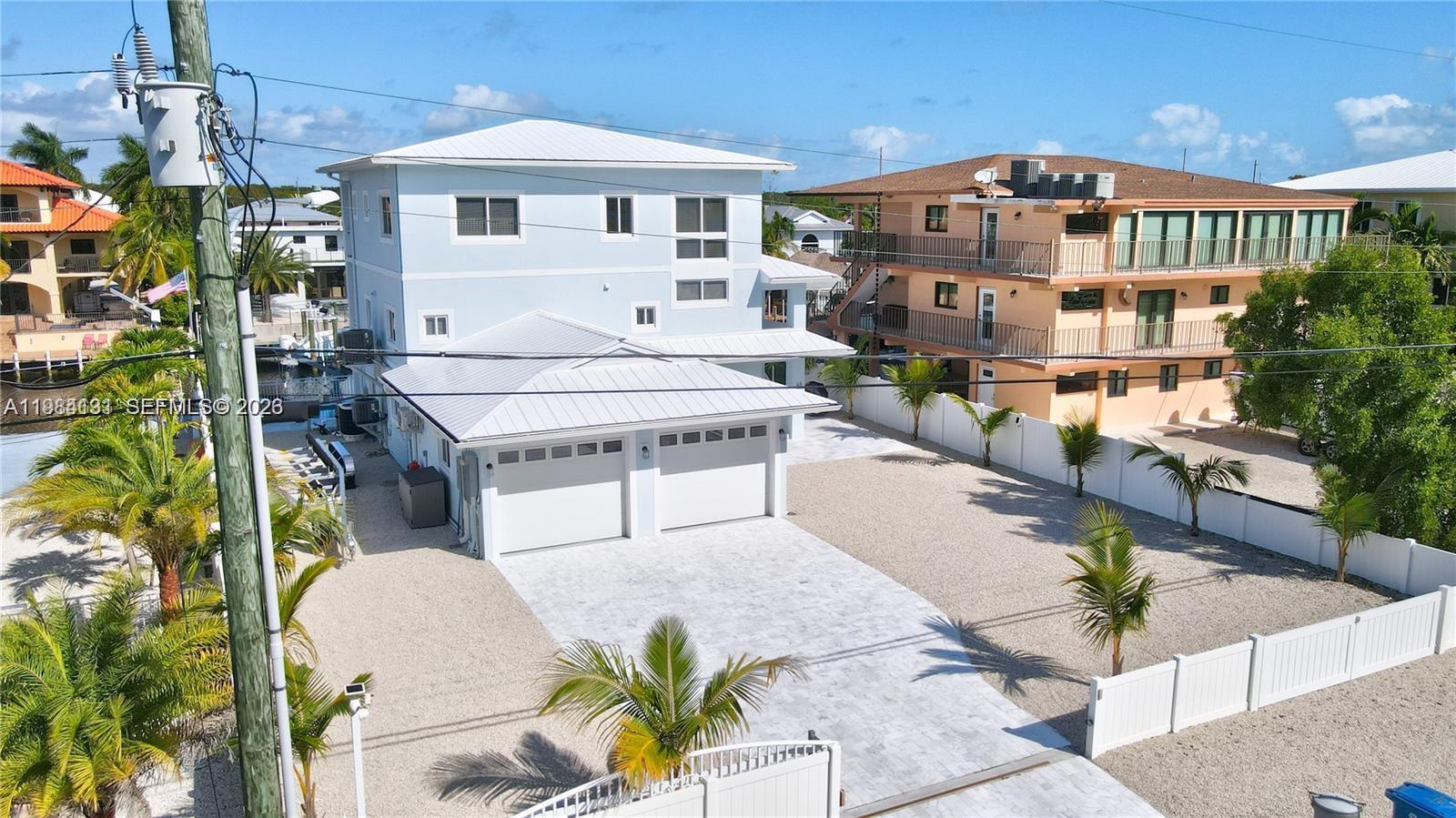 An aerial view shows a light blue three-story house with a two-car garage and driveway — 48 S Andros Rd, Key Largo FL 33037, KEY LARGO, FL