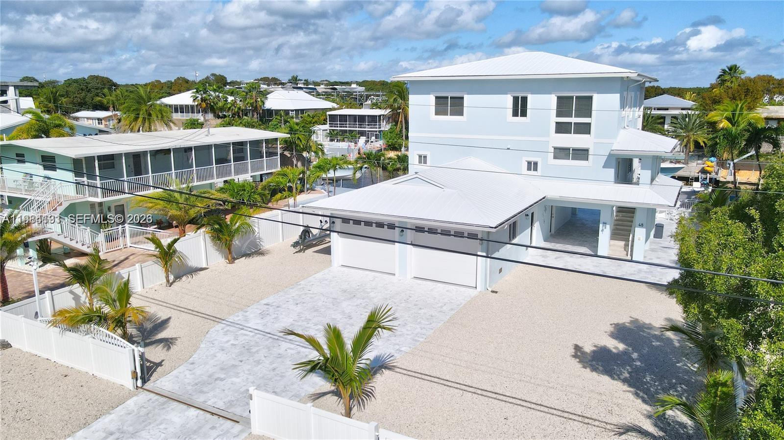 An aerial view shows a light blue multi-story house with a two-car garage and gravel driveway — 48 S Andros Rd, Key Largo FL 33037, KEY LARGO, FL