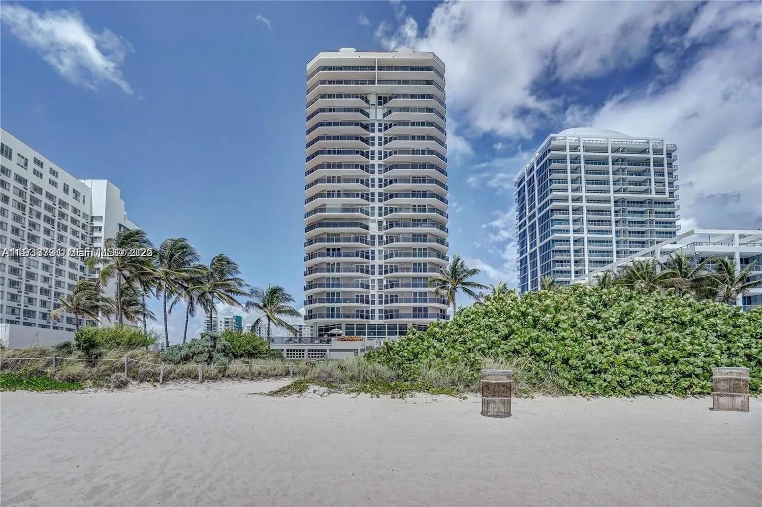 A tall residential high-rise building stands behind a sandy beach with palm trees — 6767 Collins # 901, Miami Beach FL 33141, MIAMI BEACH, FL