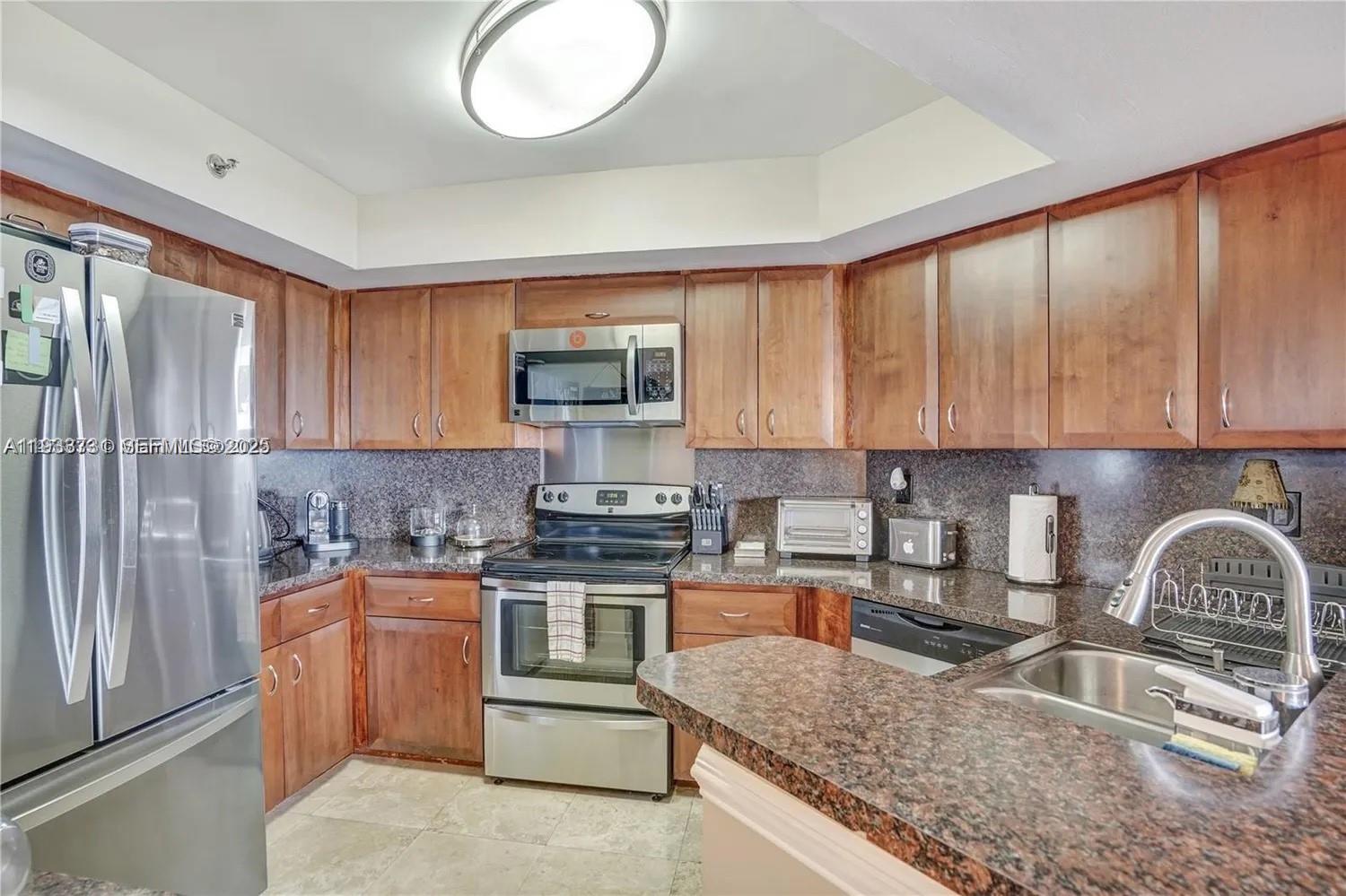 A kitchen features wood cabinets, granite countertops, stainless steel appliances, and tile flooring — 6767 Collins # 901, Miami Beach FL 33141, MIAMI BEACH, FL